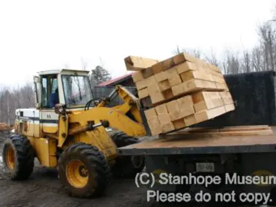 Image shows a machine unloading stacks of lumber from the back of a truck. 