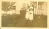 Image shows of a group of people dressed in wedding attire on the steps of a house. 