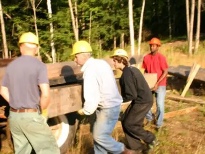 Image shows a group of people in hardhats lifting a large timber. 