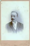 Image shows a portrait of man with with a moustache in a suit. 