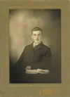 Image shows a portrait of a seated man with a book in the foreground. 