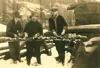 Image shows a black and white photo of three men at what appears to be a lumber camp. 