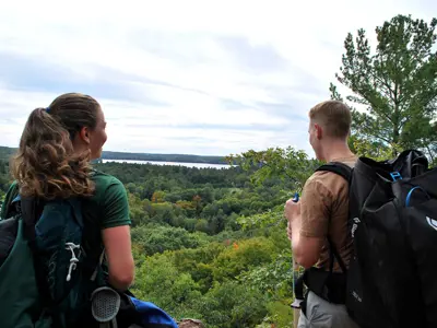 Image shows a man and woman overlooking a forested vista. 