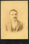 Image shows a faded portrait of man with a moustache in a suit. 