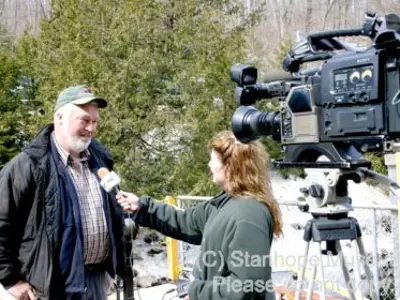 Image shows a man being interviewed by a television reporter. 