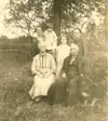 Image shows a black and white photograph of a family seated under a tree. 