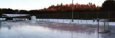 Image shows an outdoor ice rink with fence and light post. 