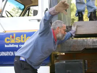 Image shows a man with a lumber truck in the background. 