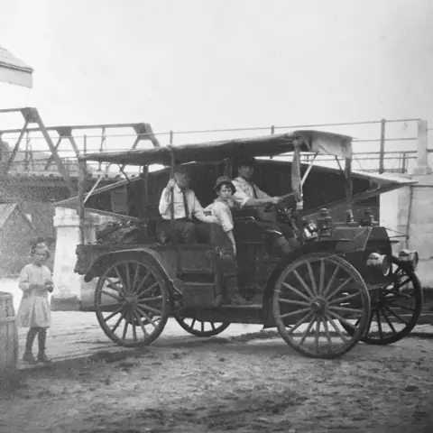 Image shows a black and white photograph of an old-fashioned automobile. 
